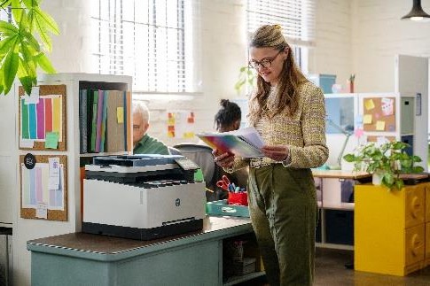 A person standing in front of a printer  Description automatically generated