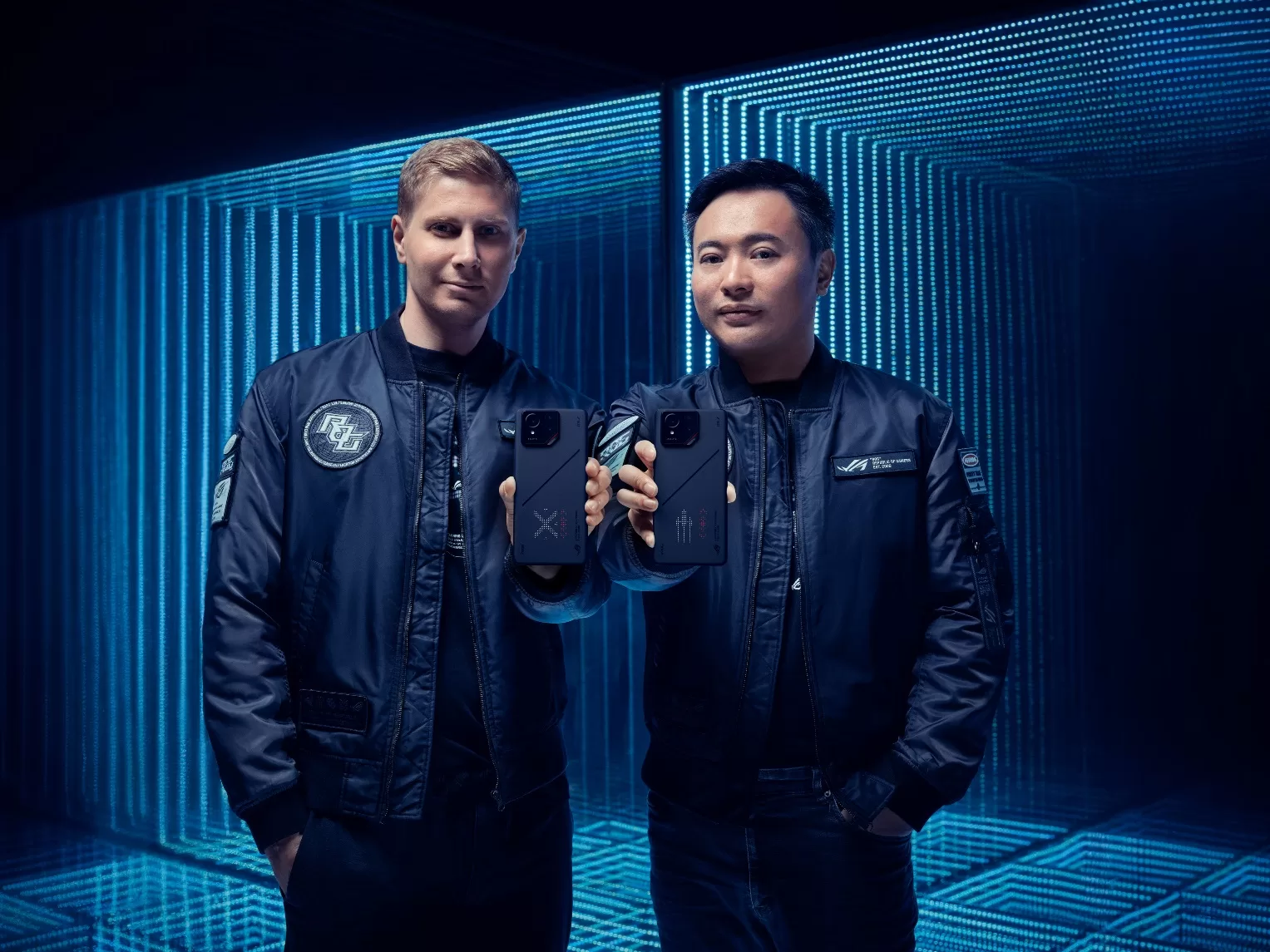 Two men in black jackets holding cell phones  Description automatically generated